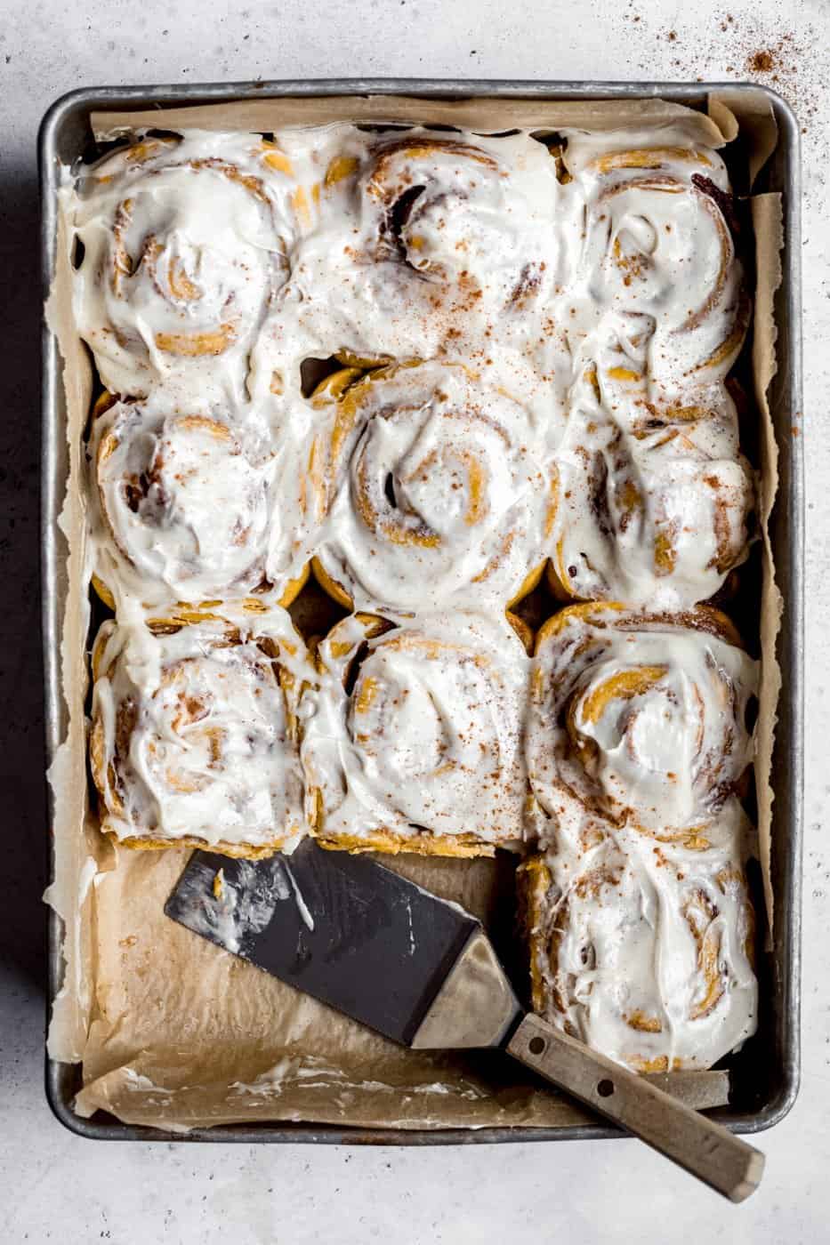 pumpkin cinnamon rolls in a pan with a spatula